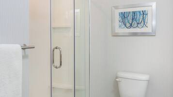 Une salle de bain avec une douche à parois de verre, des toilettes et une œuvre d’art abstraite encadrée au mur.