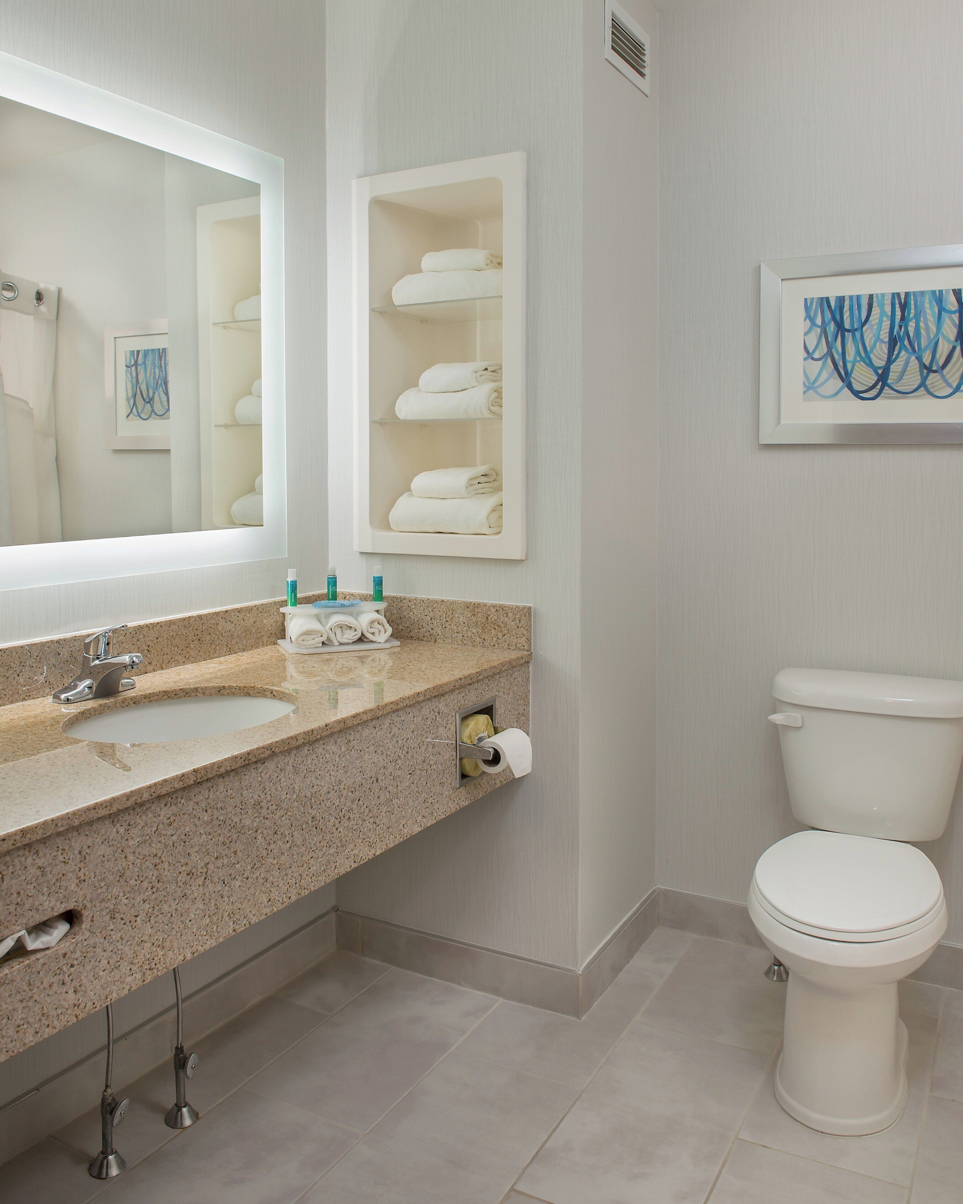 Une salle de bain moderne avec un comptoir en granit, un grand miroir, des toilettes et un porte-serviettes.