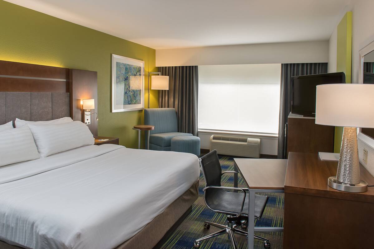 A hotel room with a large bed, a desk with a chair, a television, and a window with curtains.