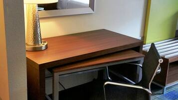 A hotel room with a wooden desk, a chair, a lamp, and a bed.