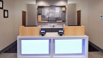 A reception desk with two digital kiosks, a large illuminated sign for Holiday Inn Express & Suites, and framed certificates on the wall.