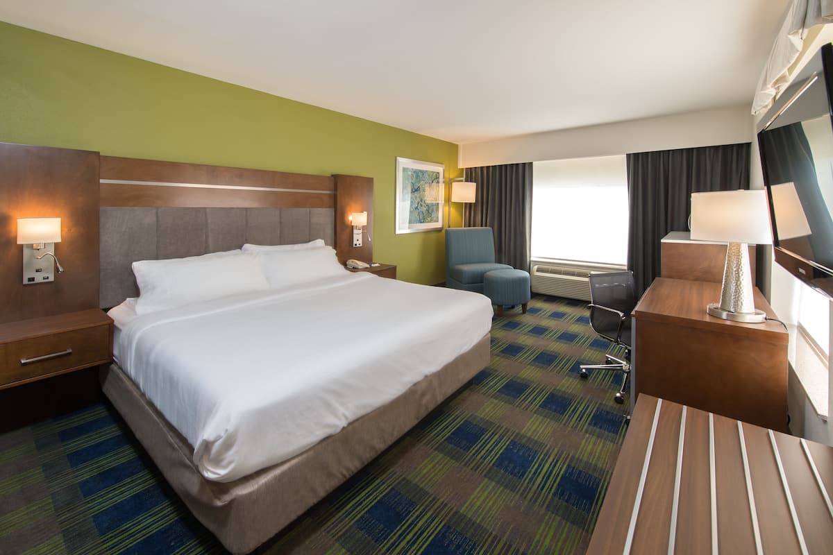 A hotel room with a large bed, a desk, a chair, and a window with curtains.