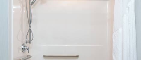 Une salle de bain moderne équipée d’une baignoire, d’une douche et de barres d’appui.