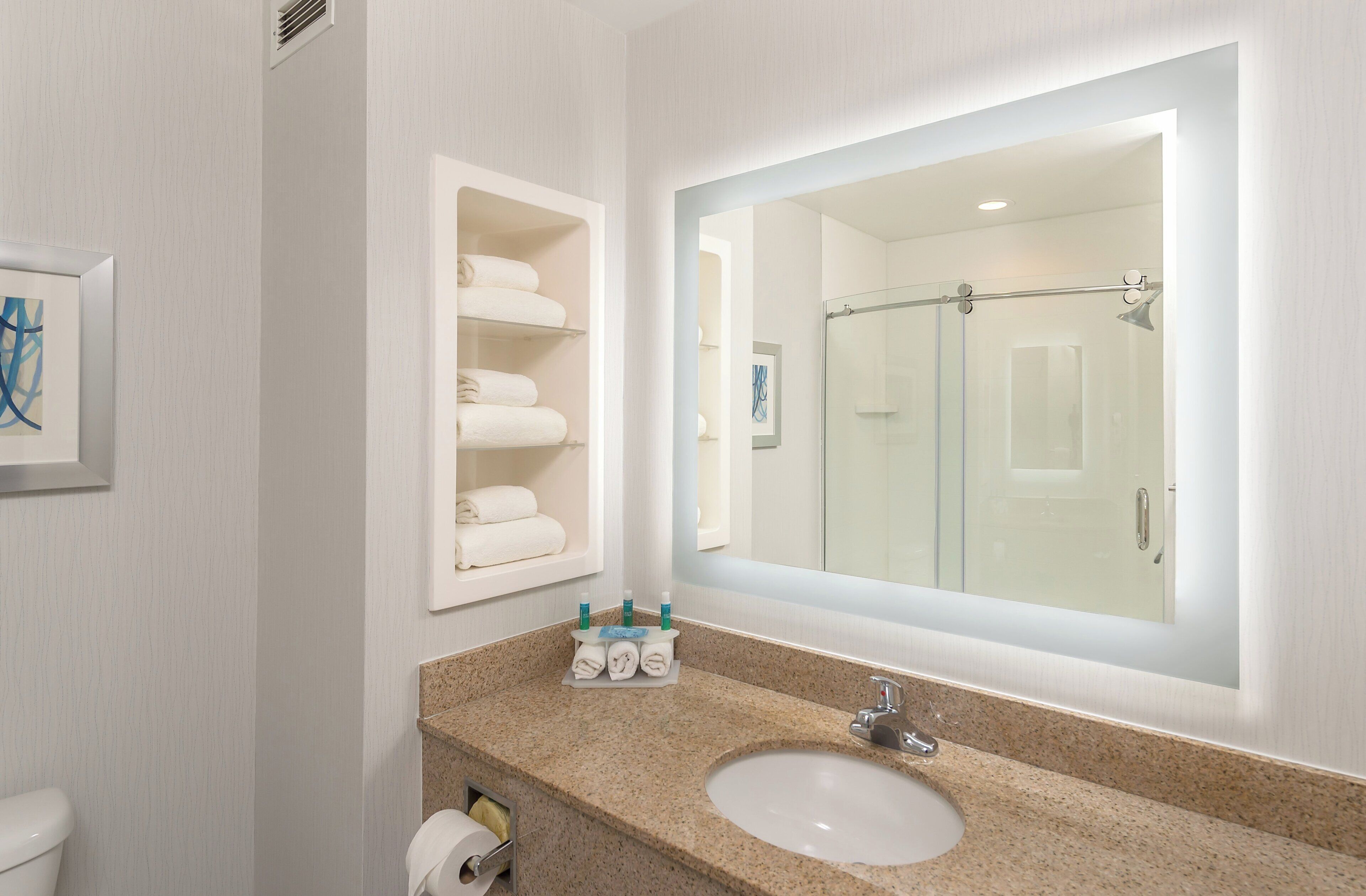 A modern bathroom with a large mirror, a sink, and a glass shower enclosure.
