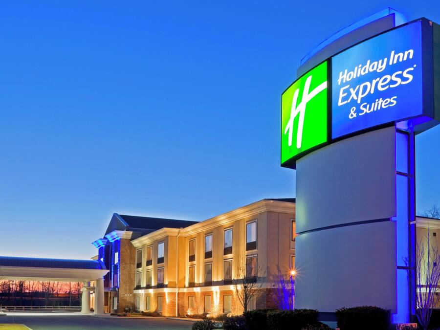 Un hotel Holiday Inn Express & Suites con un letrero iluminado llamativo, fachada de ladrillo y zona de estacionamiento techada.