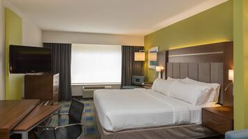 A hotel room with a large bed, a desk with chairs, a television, and a window with curtains.