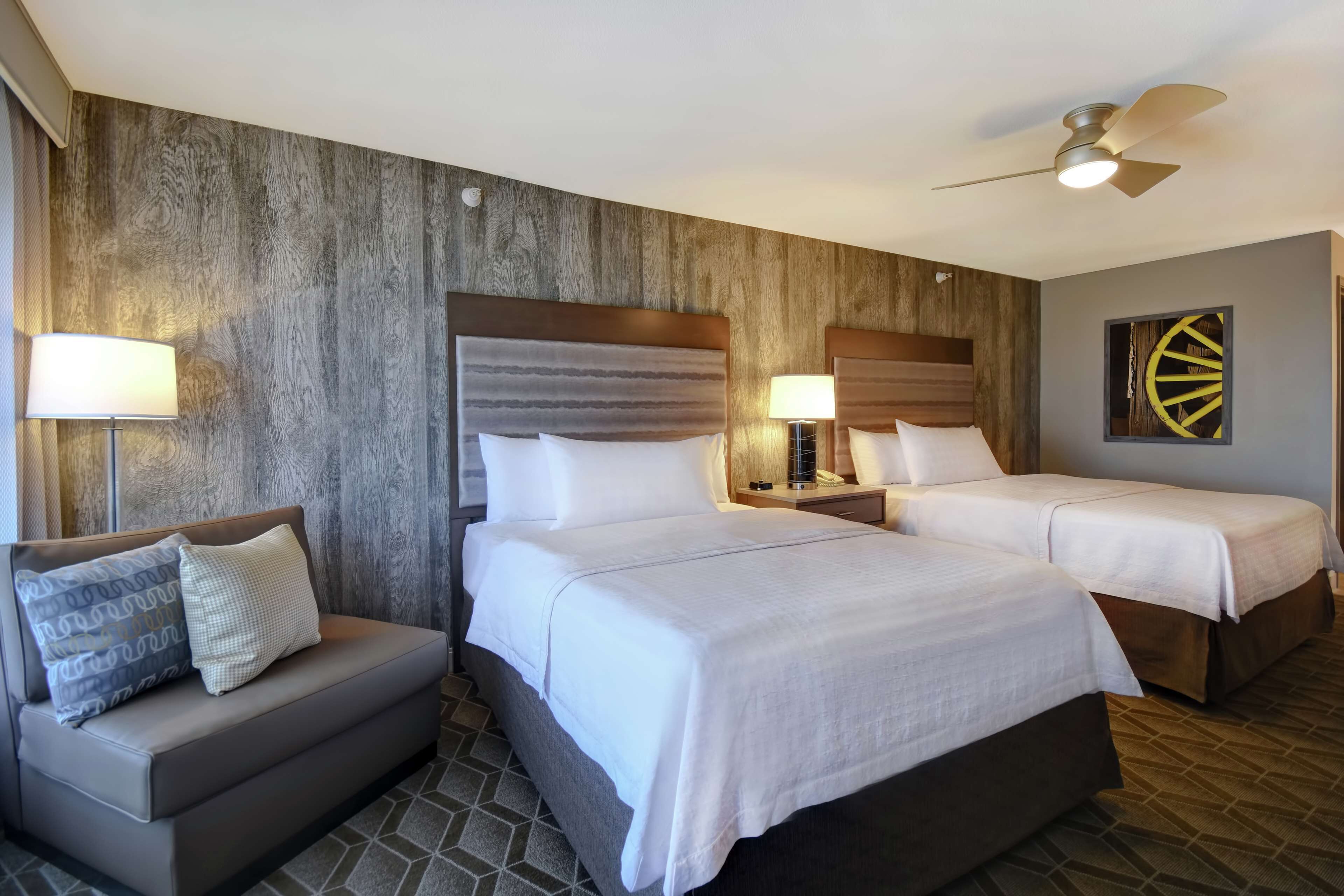 A hotel room with two beds, a sofa, and a ceiling fan.