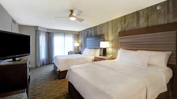 A hotel room with two beds, a television, a ceiling fan, and a large window with curtains.