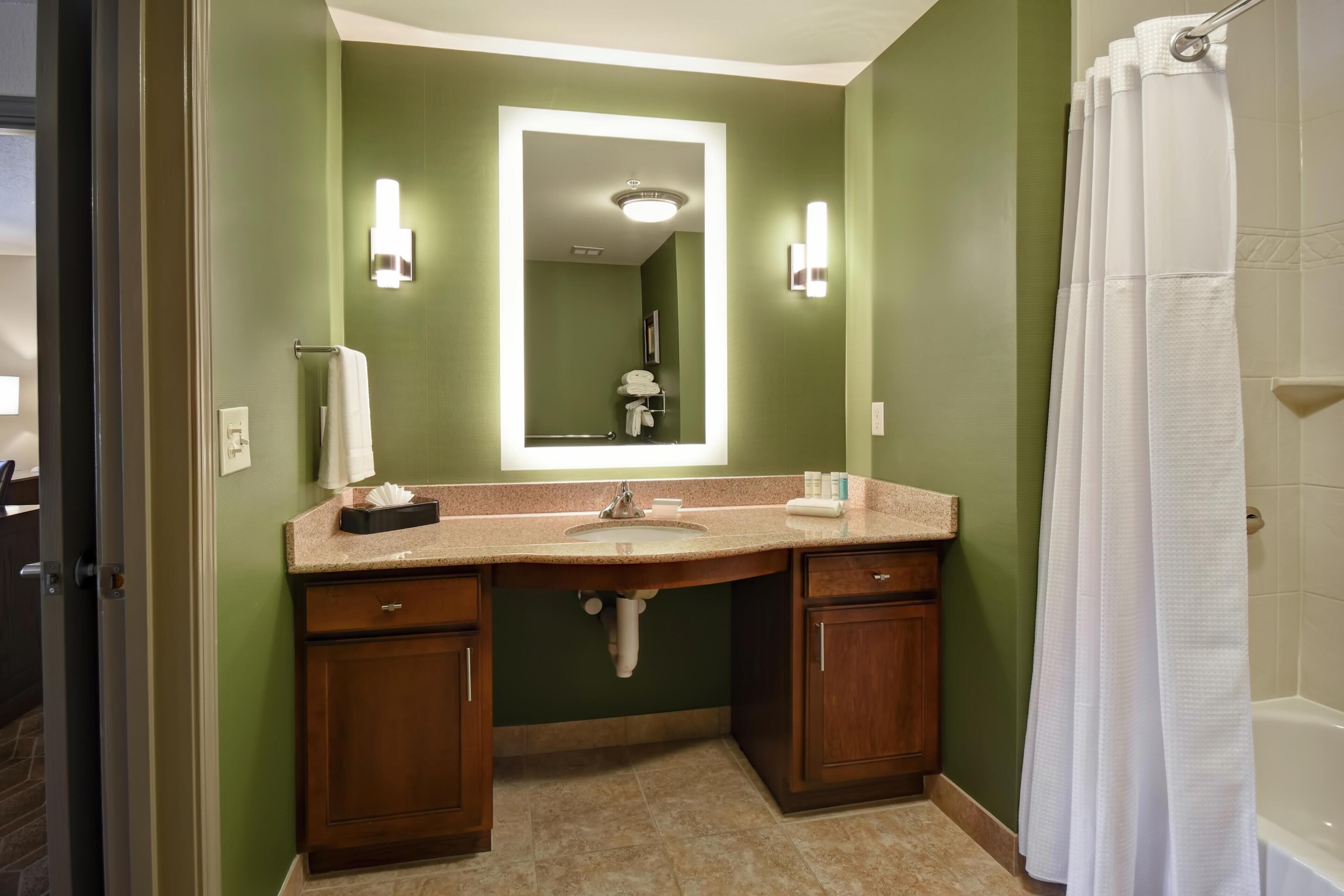 A bathroom with a sink, mirror, vanity, and shower curtain.