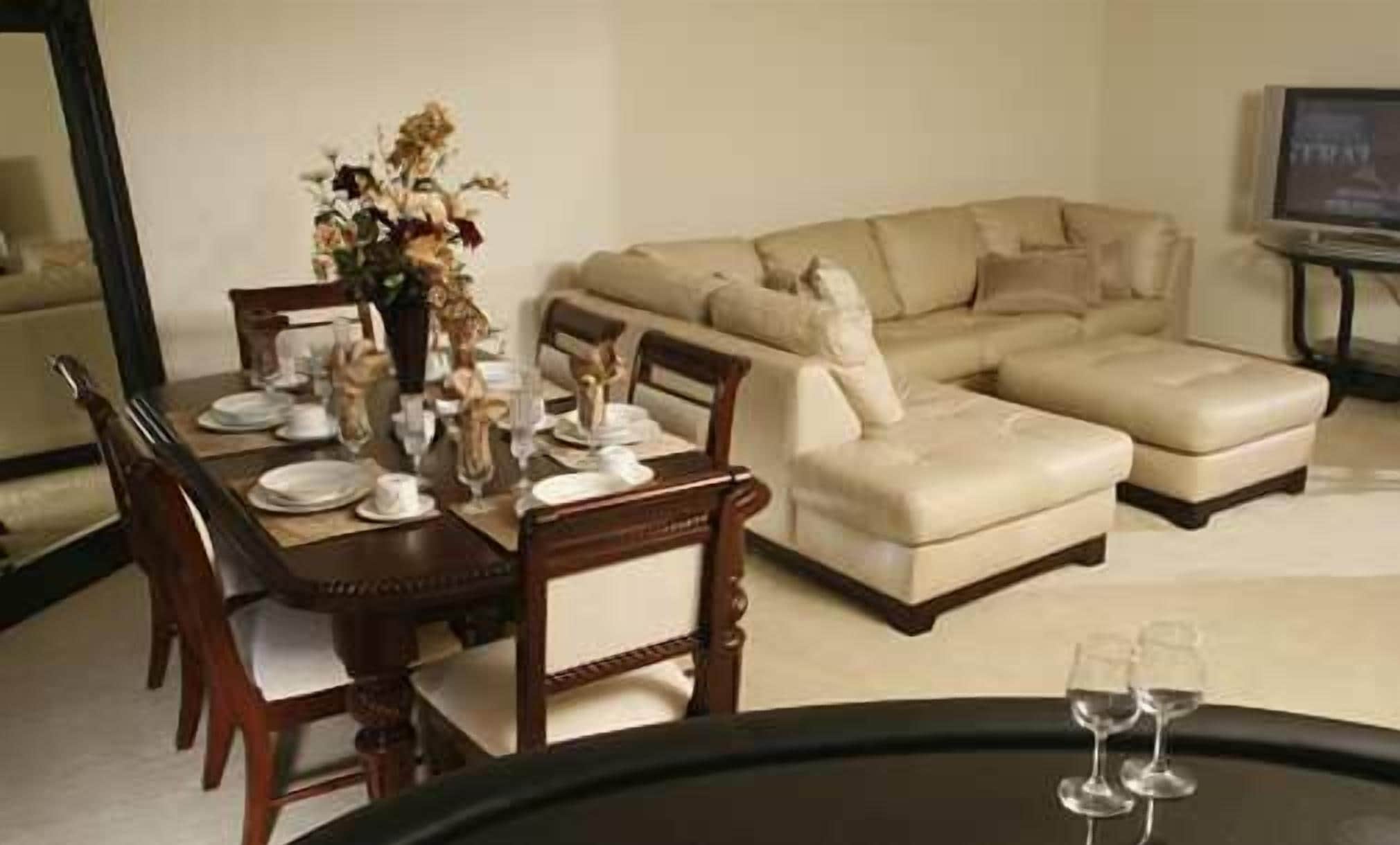 A dining area with a wooden table set for four, a beige sofa, and a television on a stand.