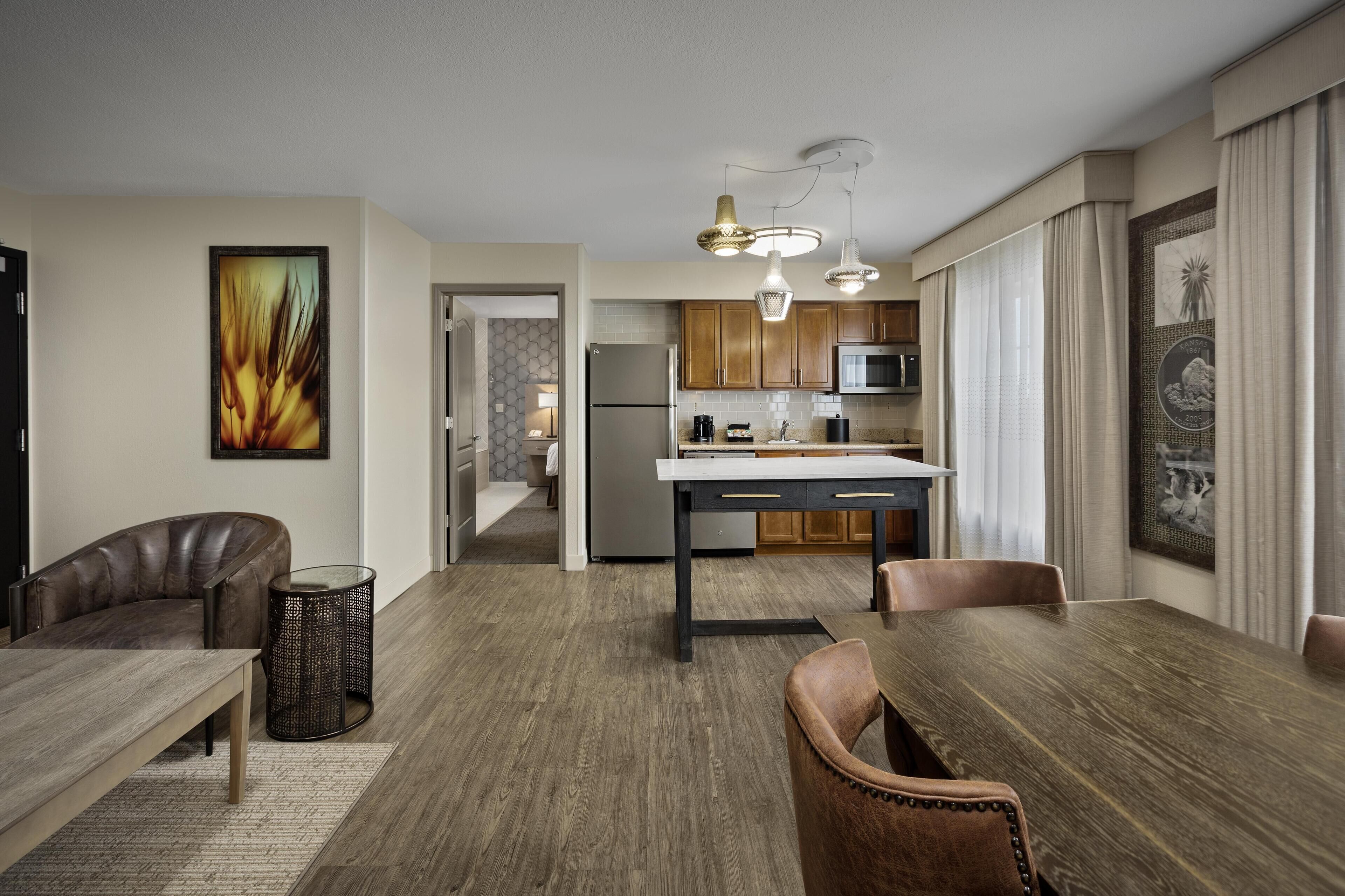 A modern kitchen with a central island, wooden dining table, and leather chairs.