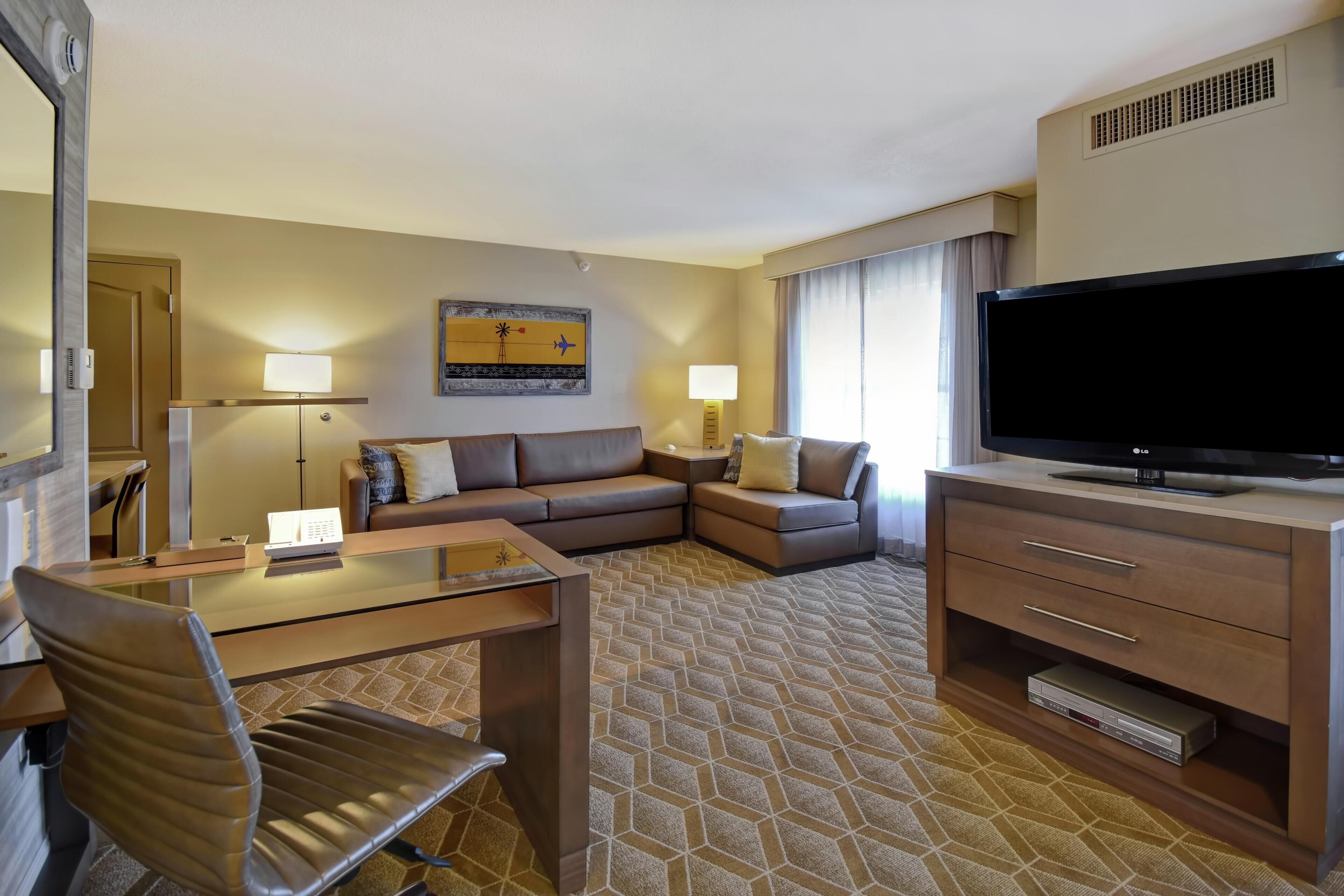 A hotel room with a sofa, a TV, a desk with a chair, and a patterned carpet.