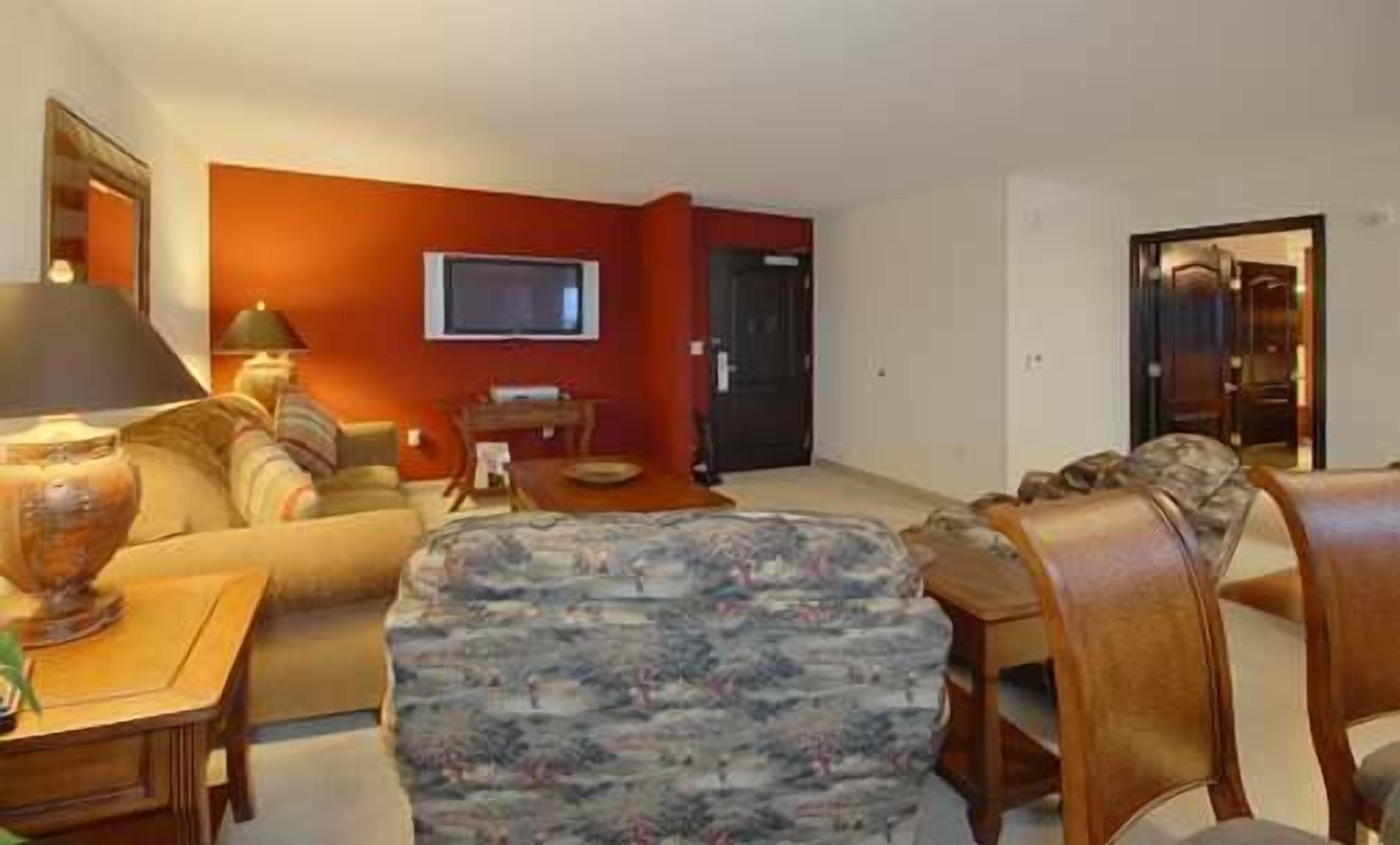 A living room with a sofa, armchair, coffee table, and a TV on the wall.