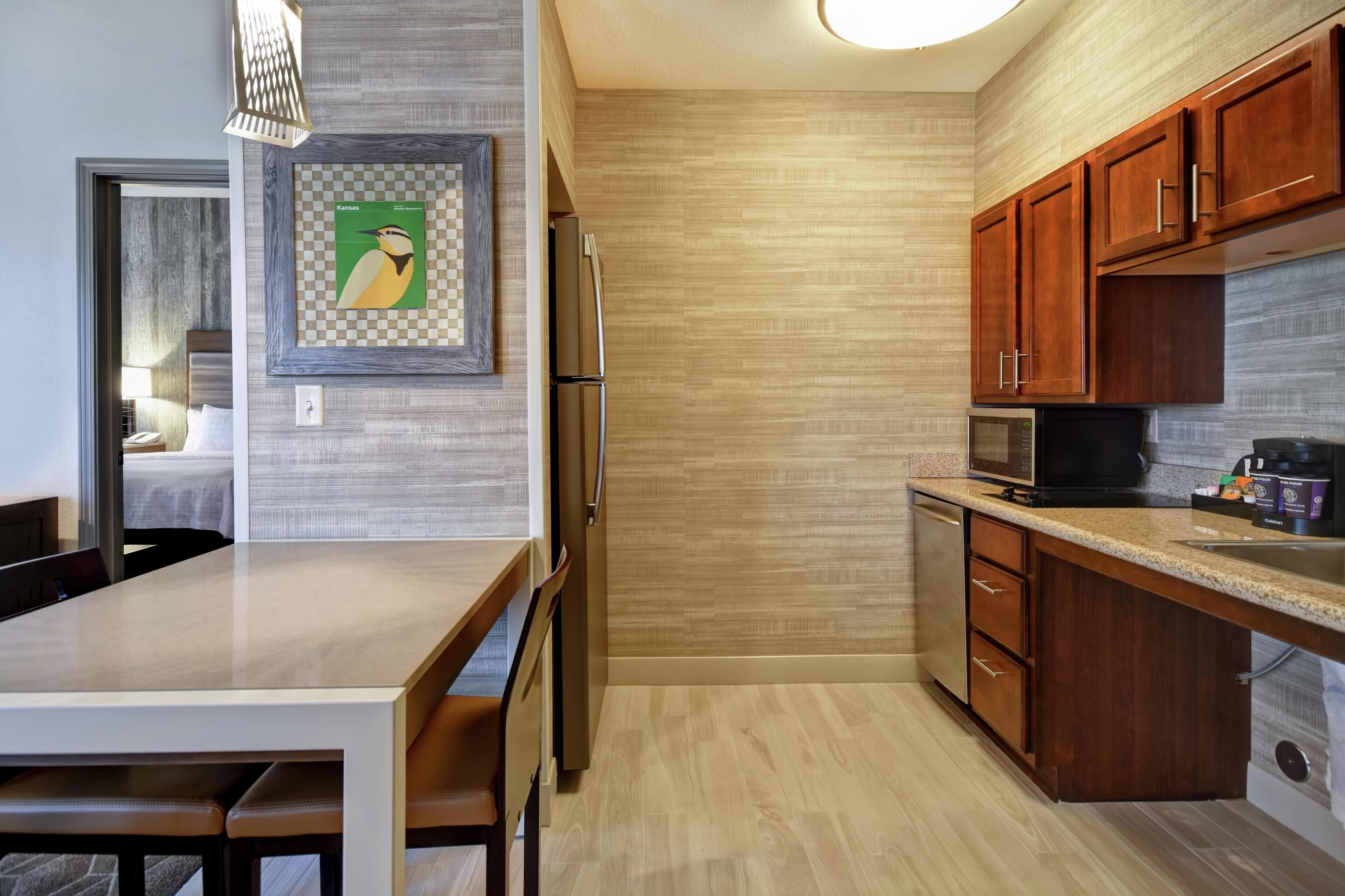 A modern kitchen with wooden cabinets, a stainless steel refrigerator, a microwave, and a dining area with a table and chairs.