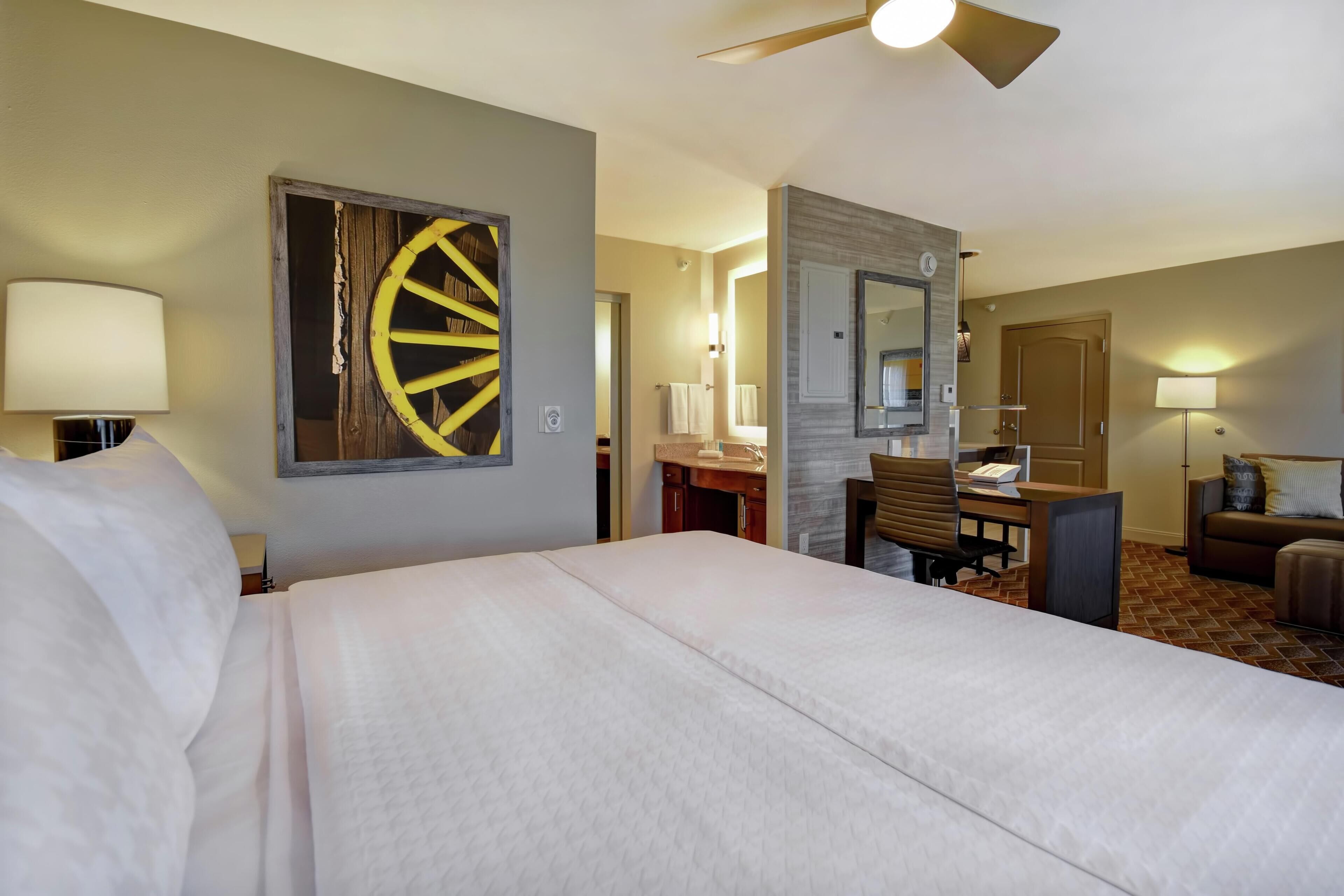 Quarto de hotel com cama, escrivaninha, cadeira e uma grande decoração na parede.