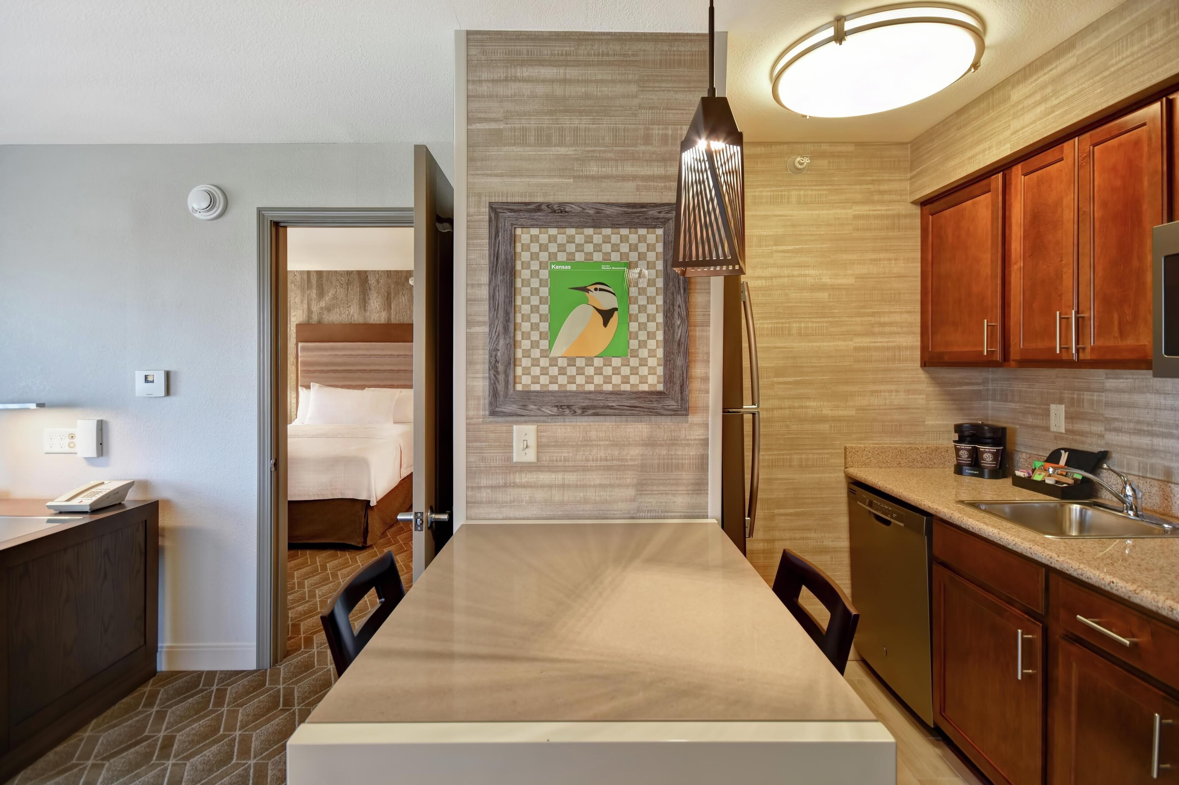 A modern kitchen with a dining table, wooden cabinets, a built-in oven, and a hanging pendant light.