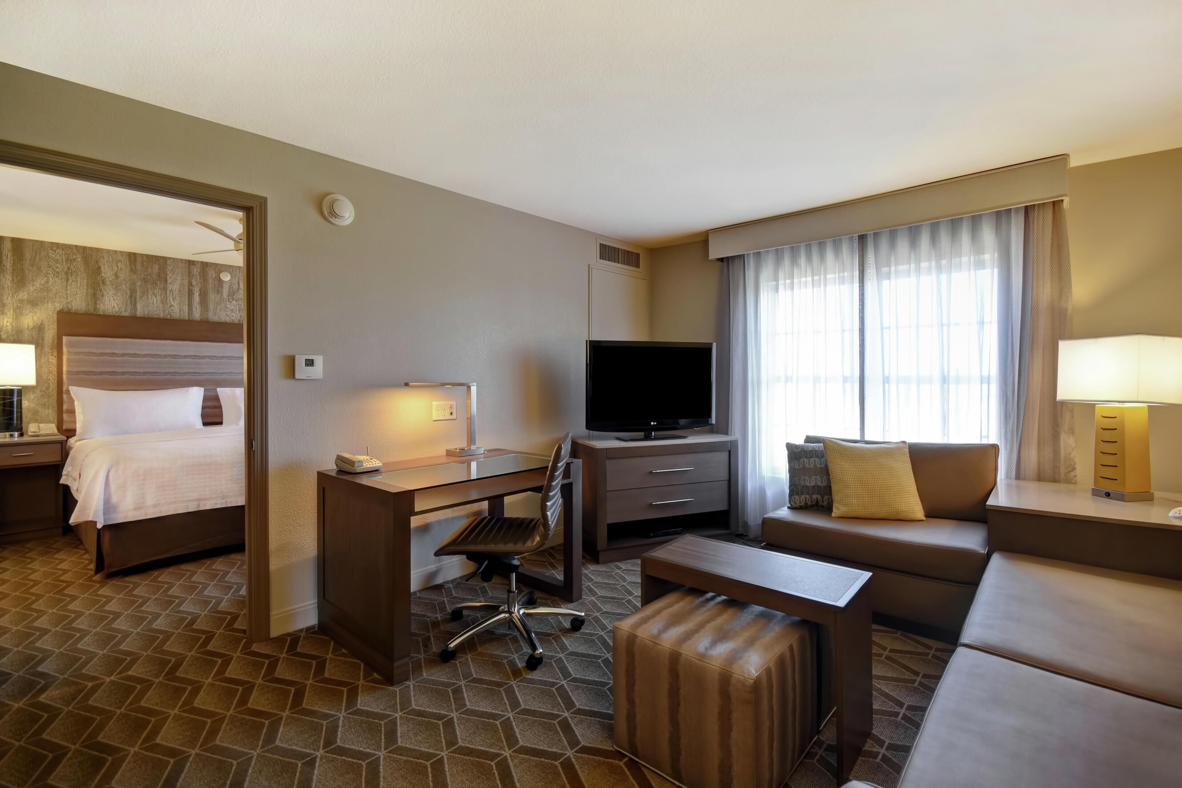 A hotel room with a bed, desk, TV, sofa, and a small table.