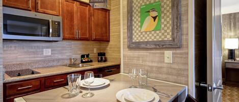 A modern kitchen with wooden cabinets, a stainless steel microwave, and a dining area set for four with plates, glasses, and cutlery.