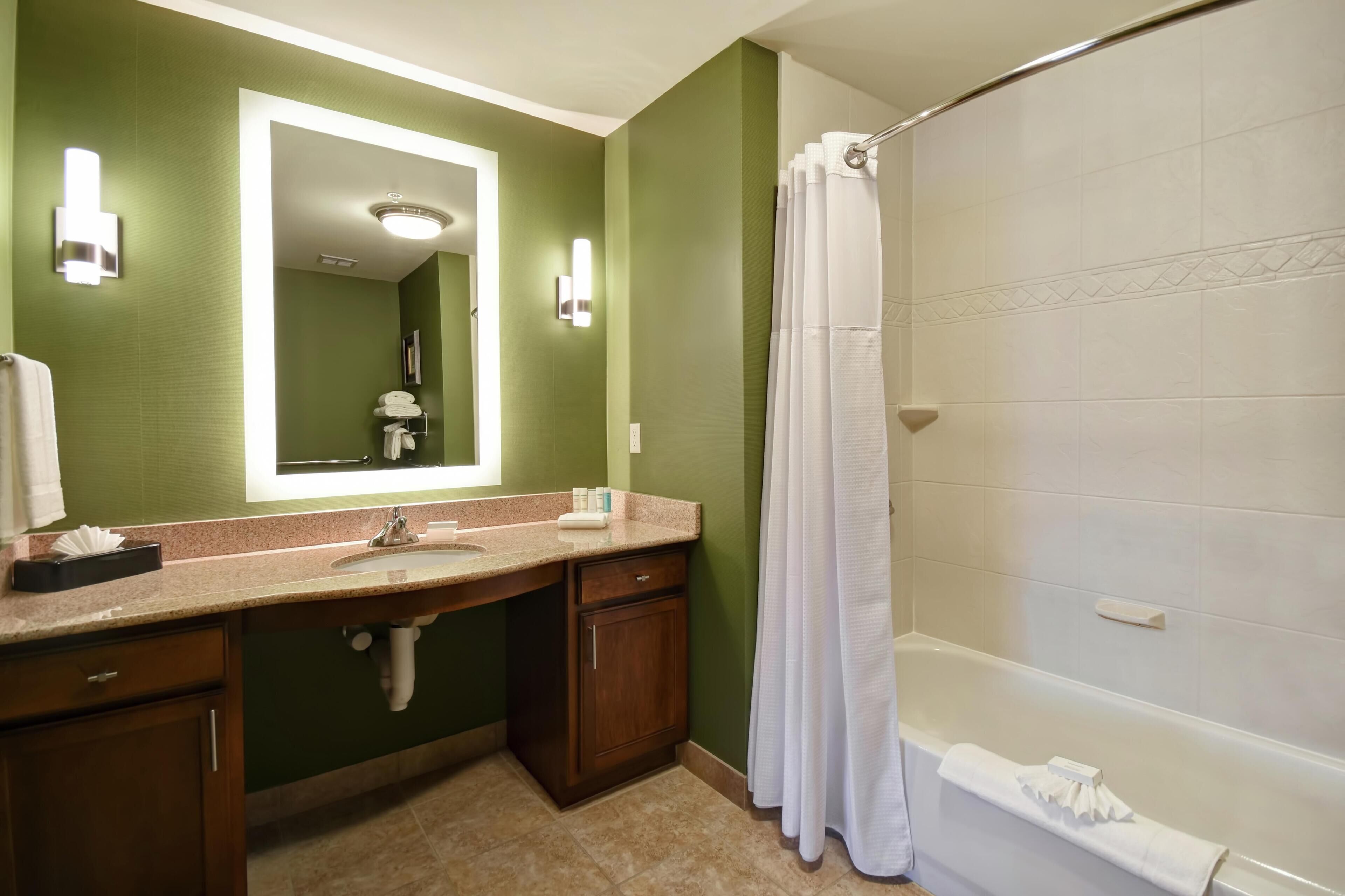 A bathroom with a green wall, a large mirror, a sink, a shower, and a bathtub.