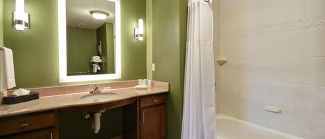 Un baño con pared verde, un espejo grande, un lavabo, ducha y bañera.