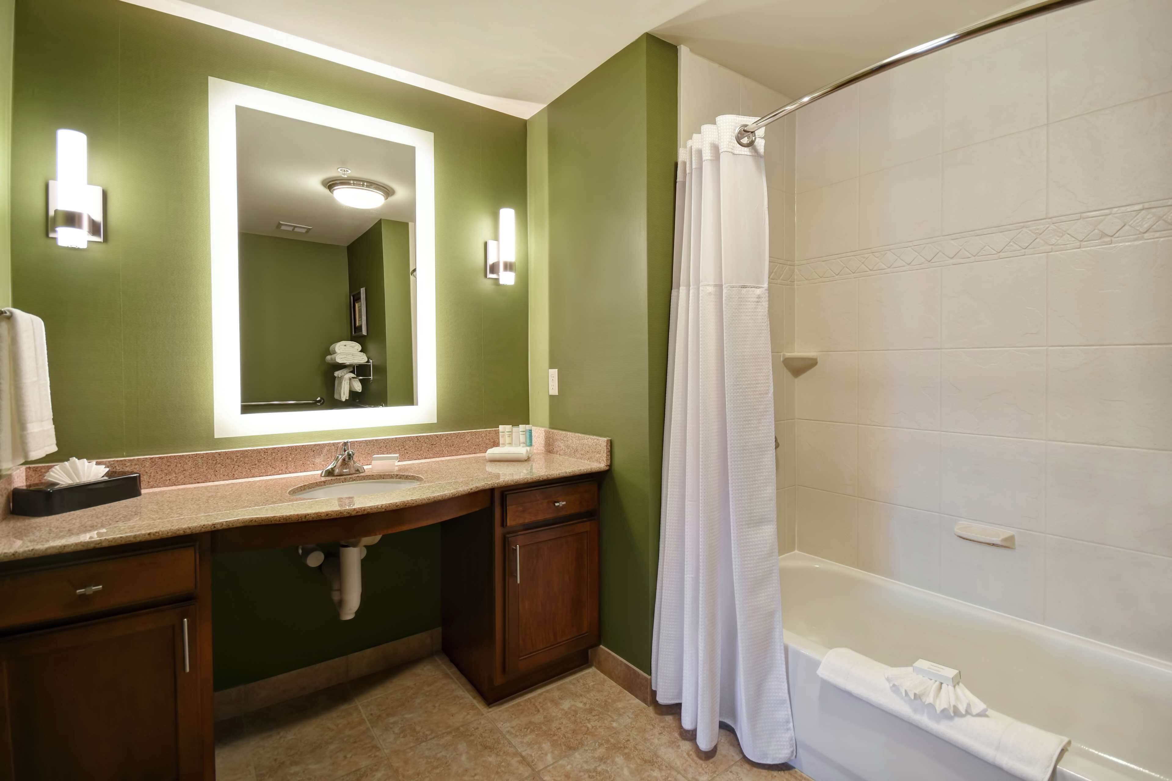 A bathroom with a green wall, a large mirror, a sink, a shower, and a bathtub.