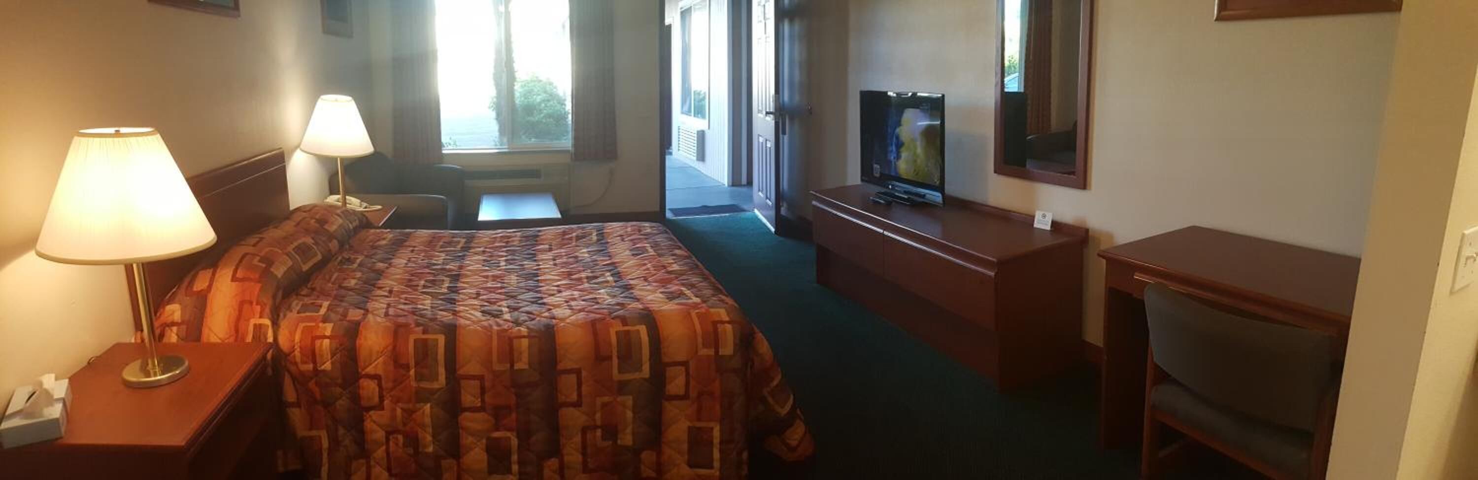Una habitación de hotel con una cama, un escritorio, una silla, un televisor y una ventana.