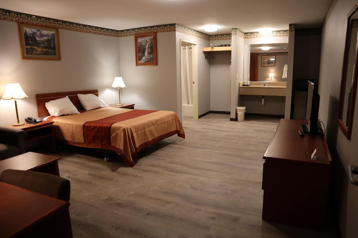 A hotel room with a bed, bedside tables, a desk, a mirror, and a bathroom with a shower and sink.