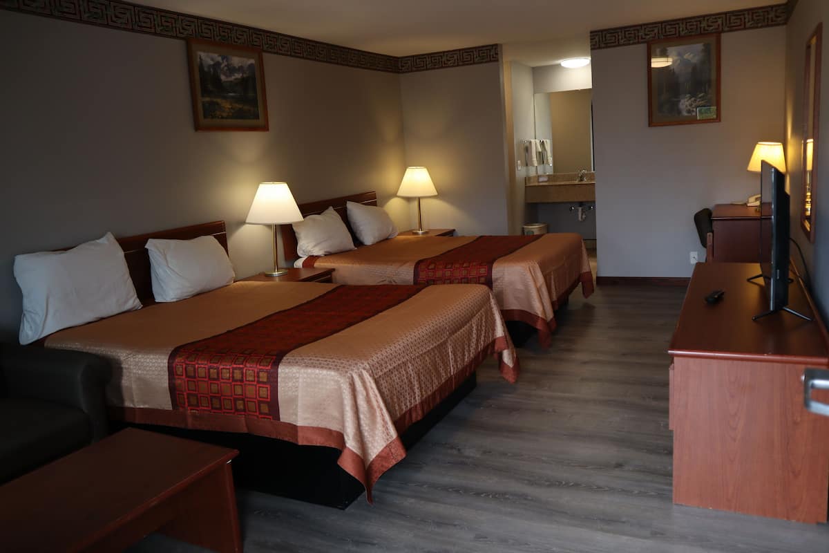 A hotel room with three beds, each with a red and white bedspread, two bedside lamps, a wooden desk, and a television.