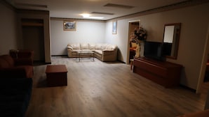 Una sala de estar con un sofá color beige, una mesa de centro, un televisor sobre un soporte de madera y un espejo en la pared.