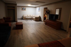 Una sala de estar con un sofá color beige, una mesa de centro, un televisor sobre un soporte de madera y un espejo en la pared.