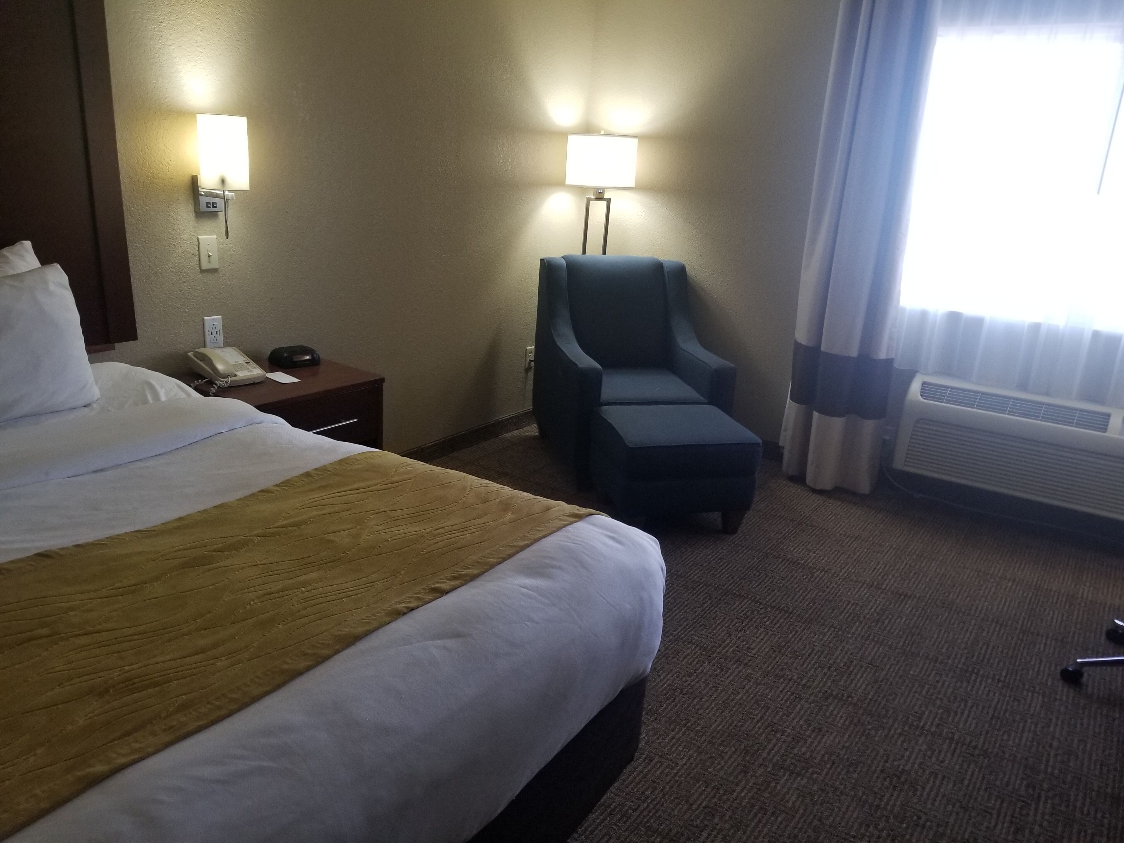 Habitación de hotel con una cama grande, lámparas de noche, una silla, un teléfono y un equipo de aire acondicionado.