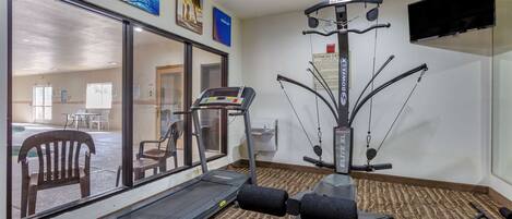 A fitness center with a treadmill, BowFlex, and a mirrored wall.