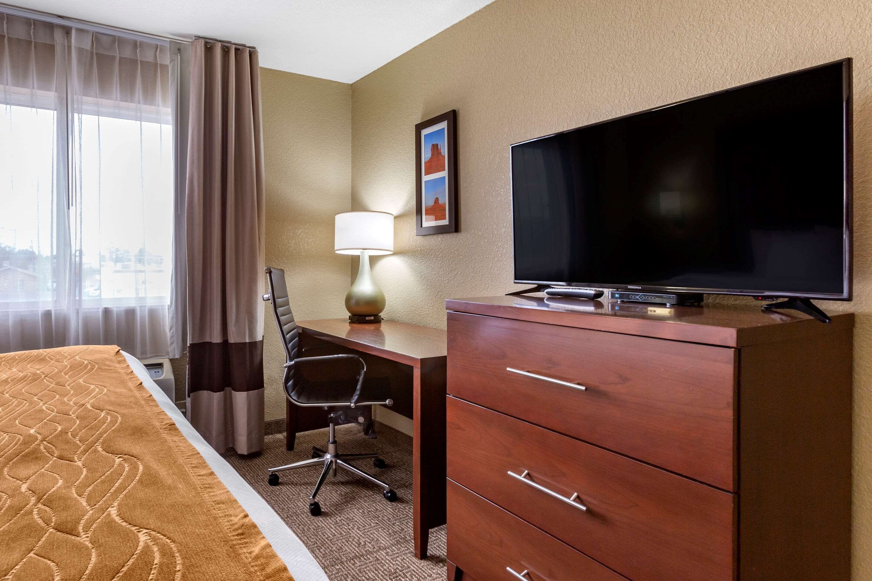 A hotel room with a bed, a desk with a chair, a television, and a dresser.