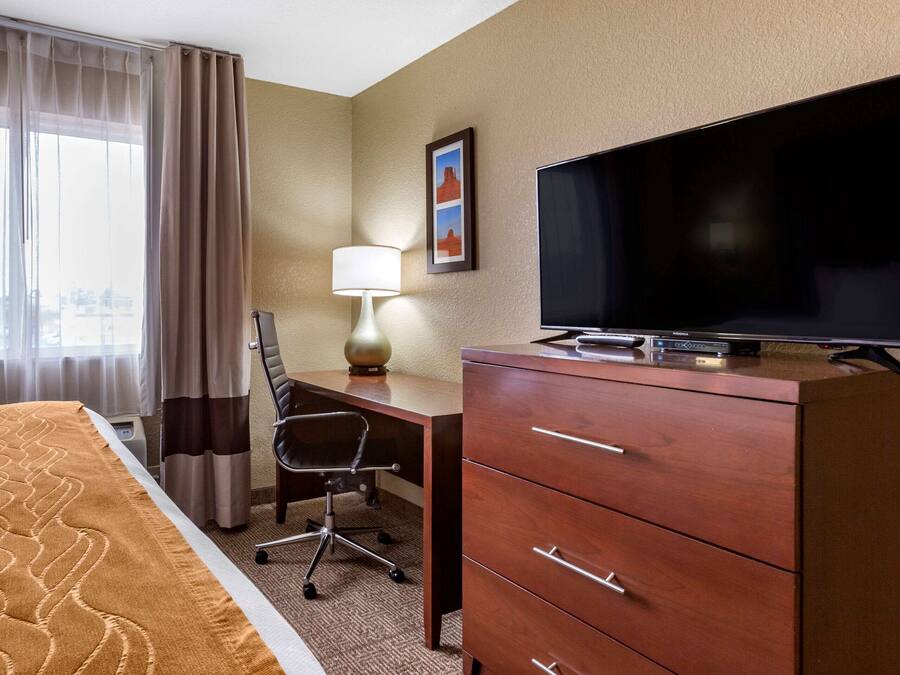 A hotel room with a bed, a desk with a chair, a television, and a dresser.