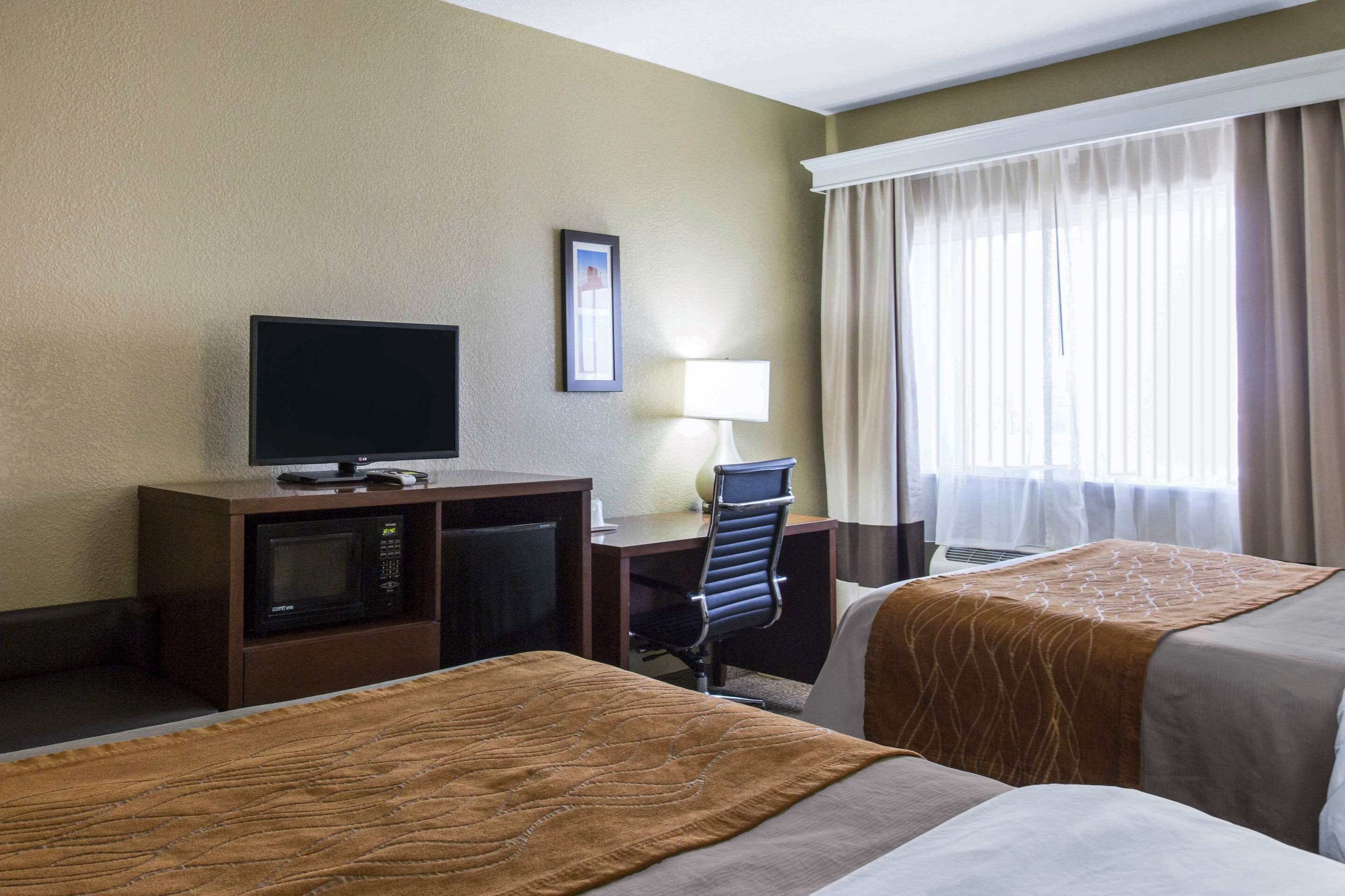 Una habitación de hotel con dos camas, un escritorio con ordenador, televisor y microondas.