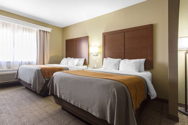A hotel room with two beds, a large window with curtains, an air conditioning unit, and a wall-mounted lamp.