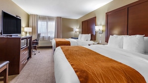 A hotel room with two beds, a desk with a TV, and a view of the outdoors through the window.