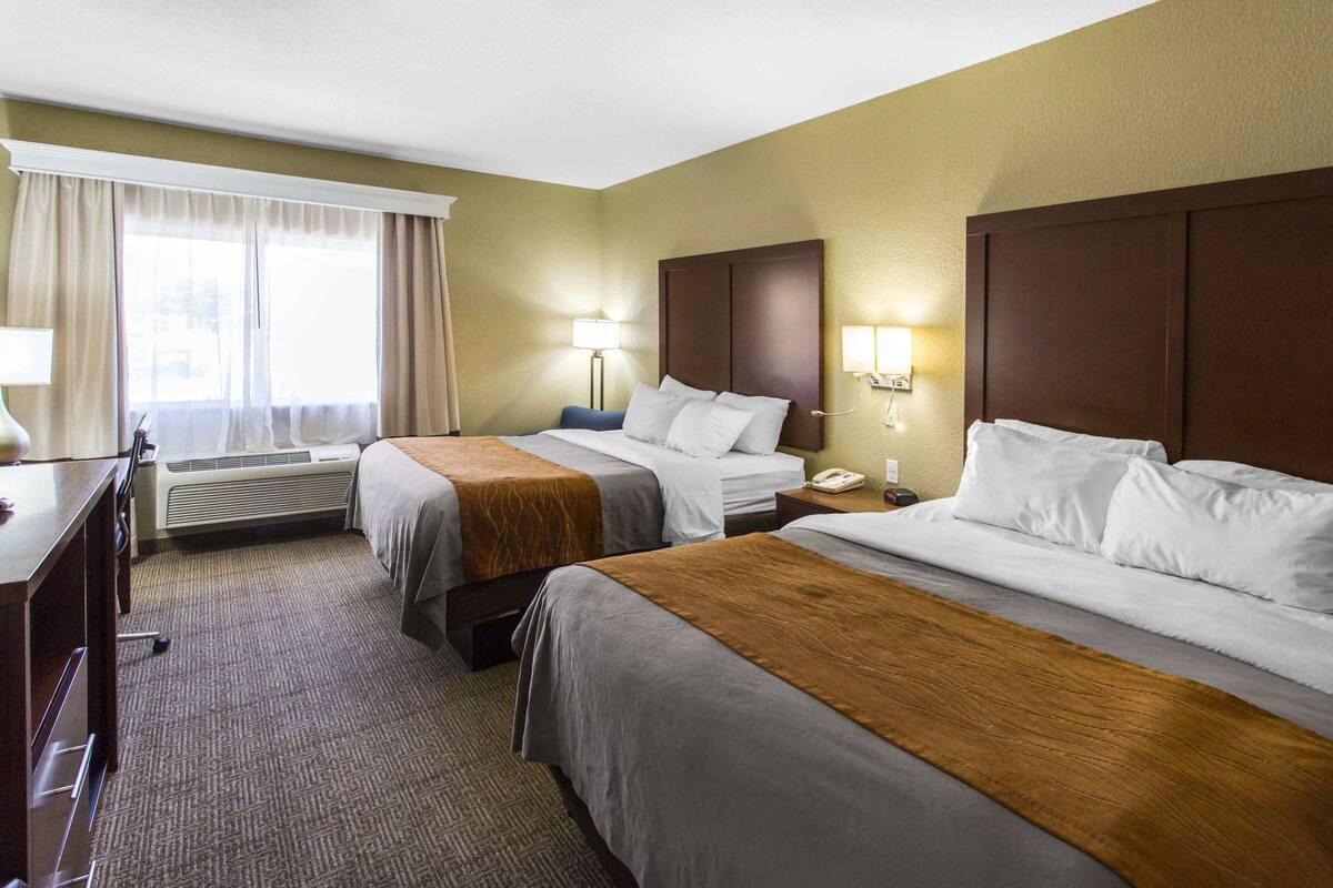 A hotel room with two beds, a desk, and a window with curtains.