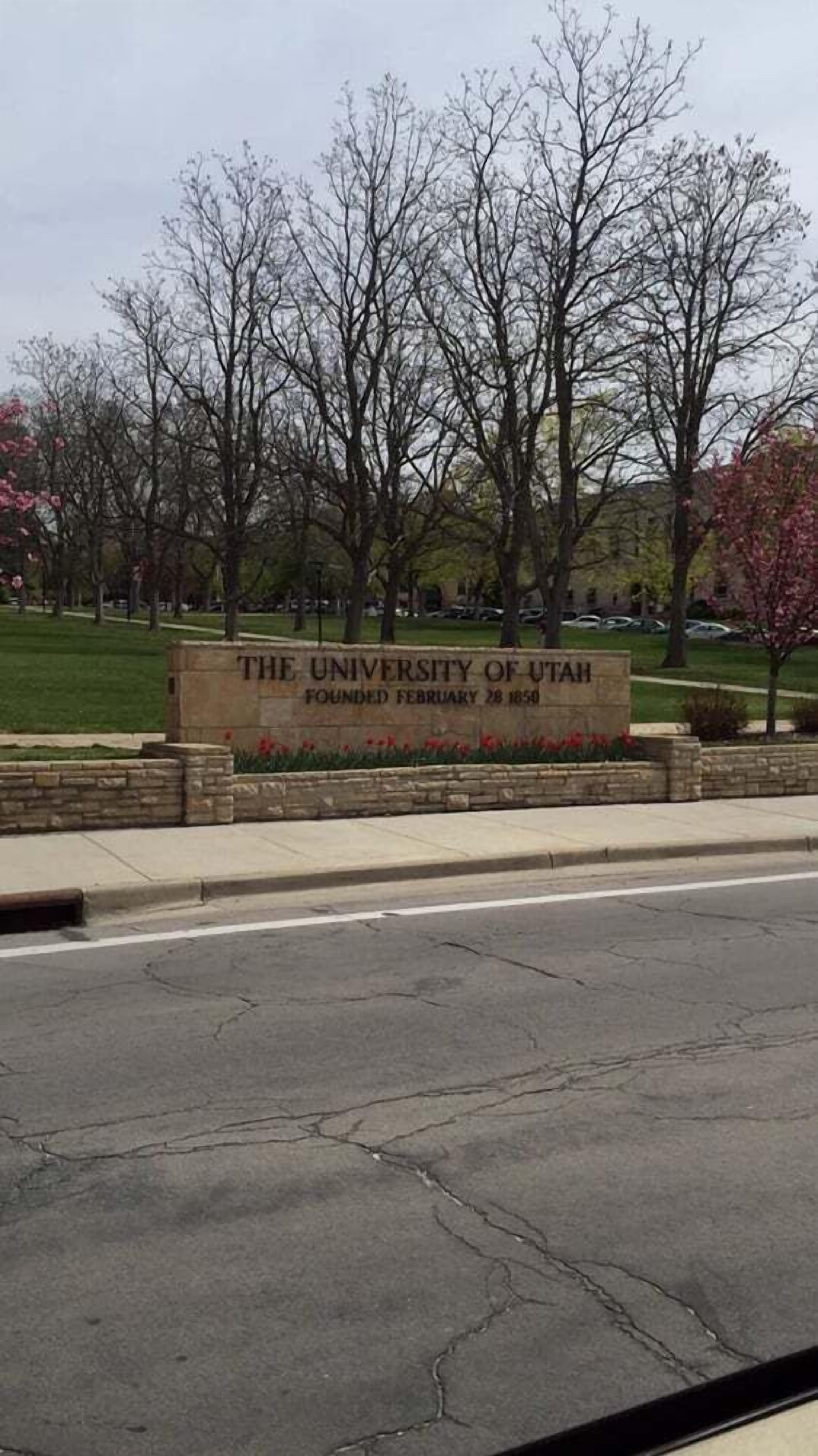 Een stenen bord met de tekst 'The University of Utah Opgericht 28 februari 1850', omringd door bomen en een gazon.