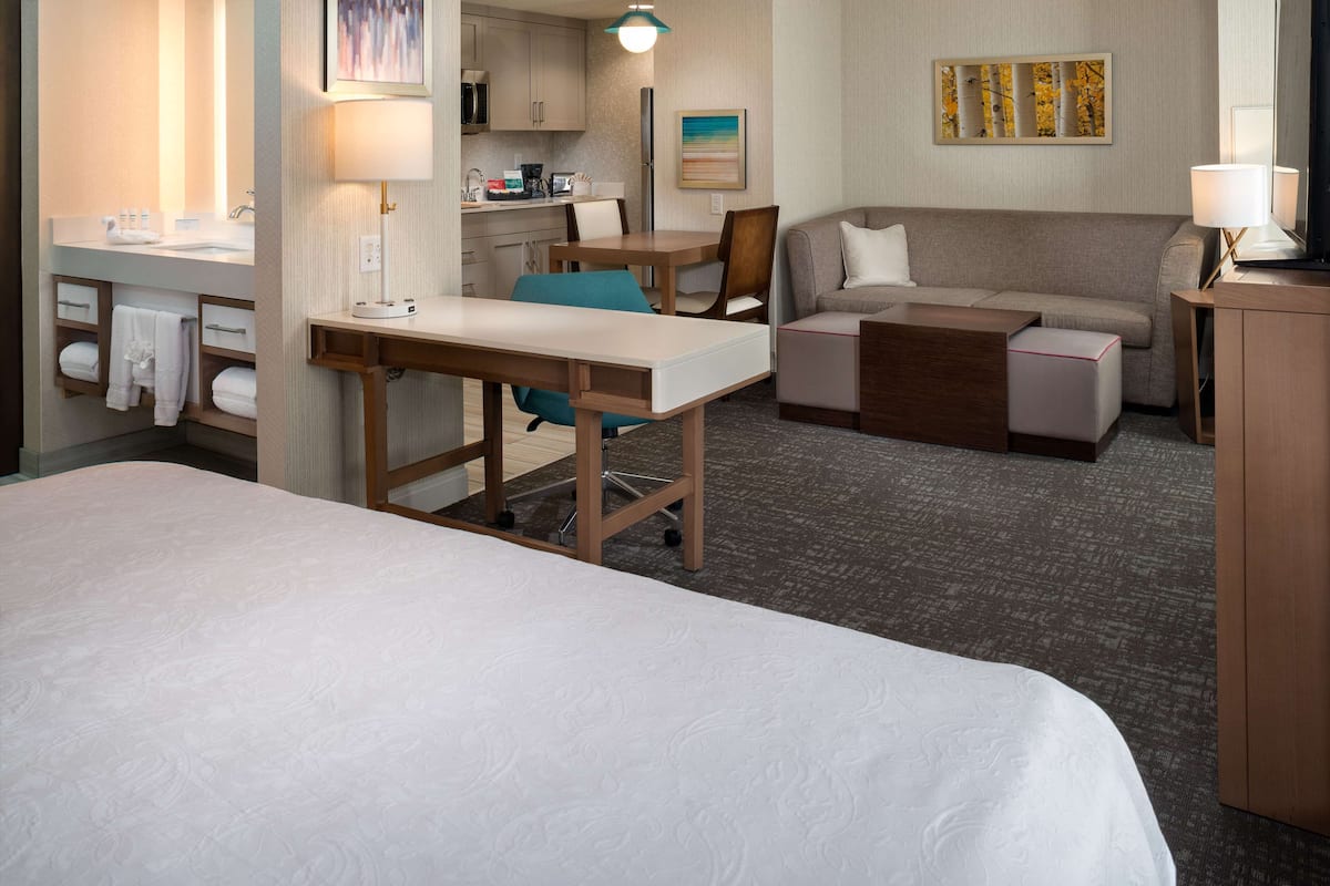 Una camera d'albergo con un letto, una scrivania, un divano, un angolo cottura e un bagno con lavandino e portasciugamani.