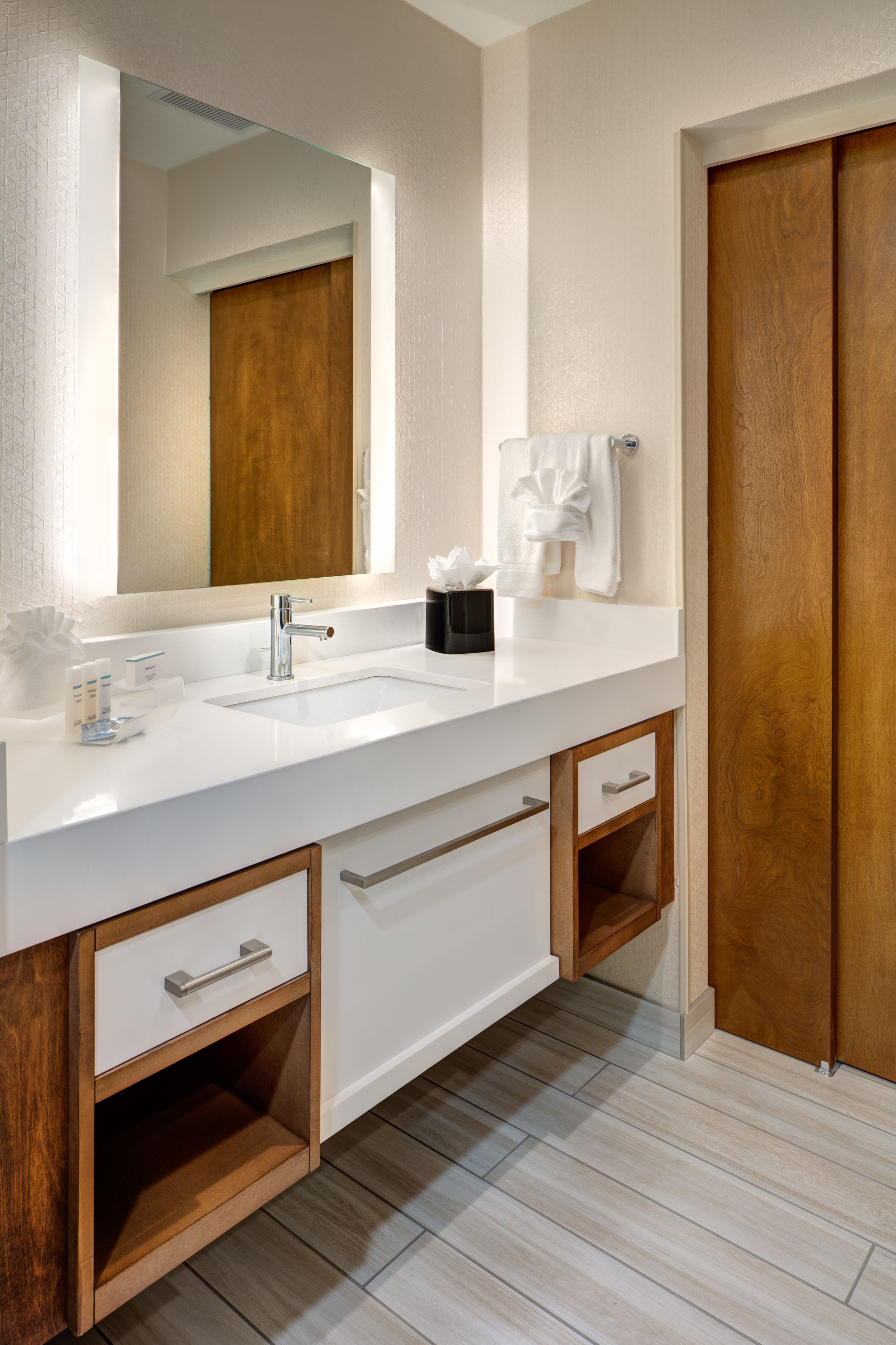 A modern bathroom with a white sink, a large mirror, and wooden cabinets.