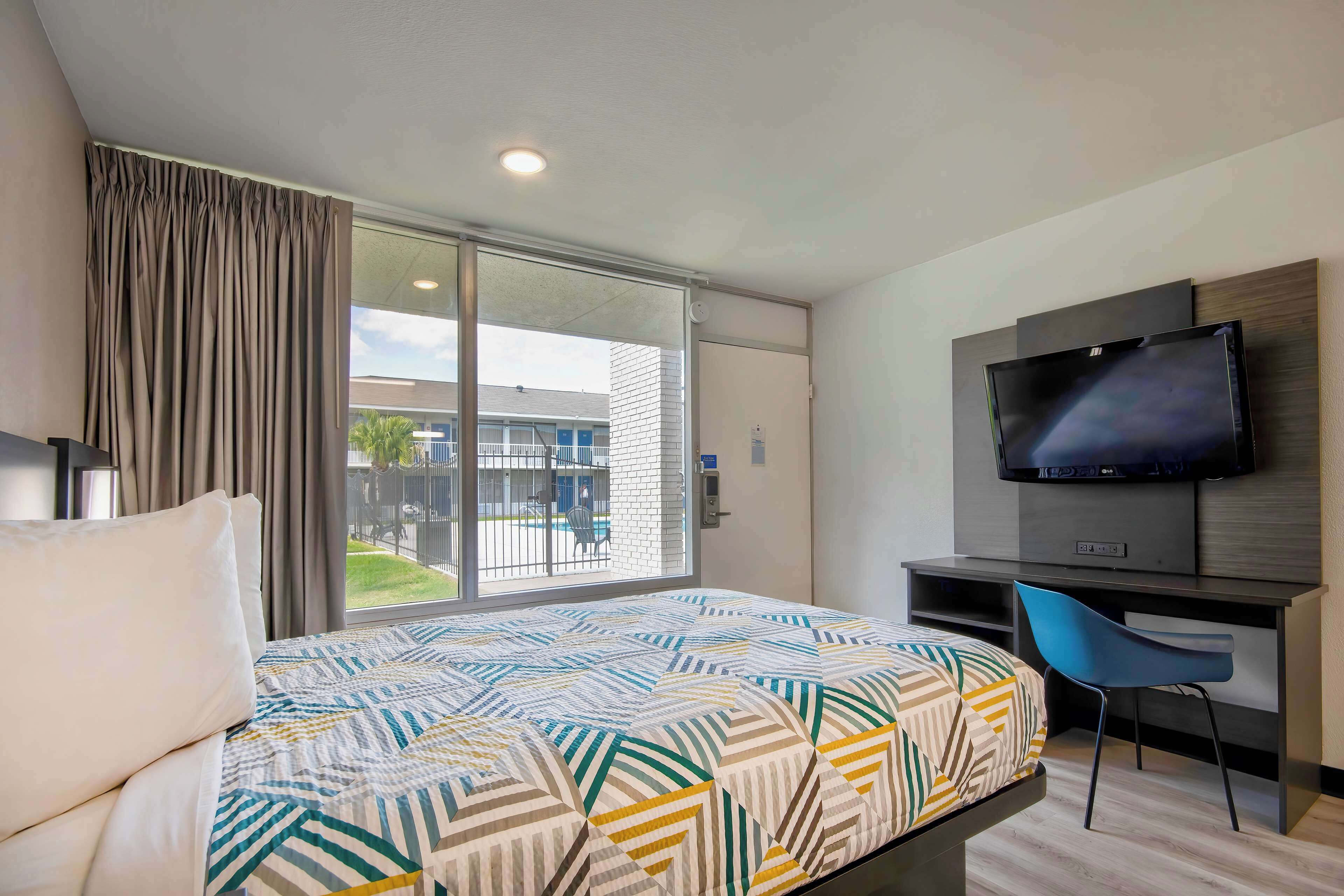 A hotel room with a bed, a desk, a chair, a television, and a sliding glass door to the outside.