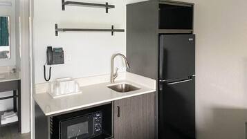 Una cocina compacta con microondas integrado, un lavamanos y un refrigerador negro.