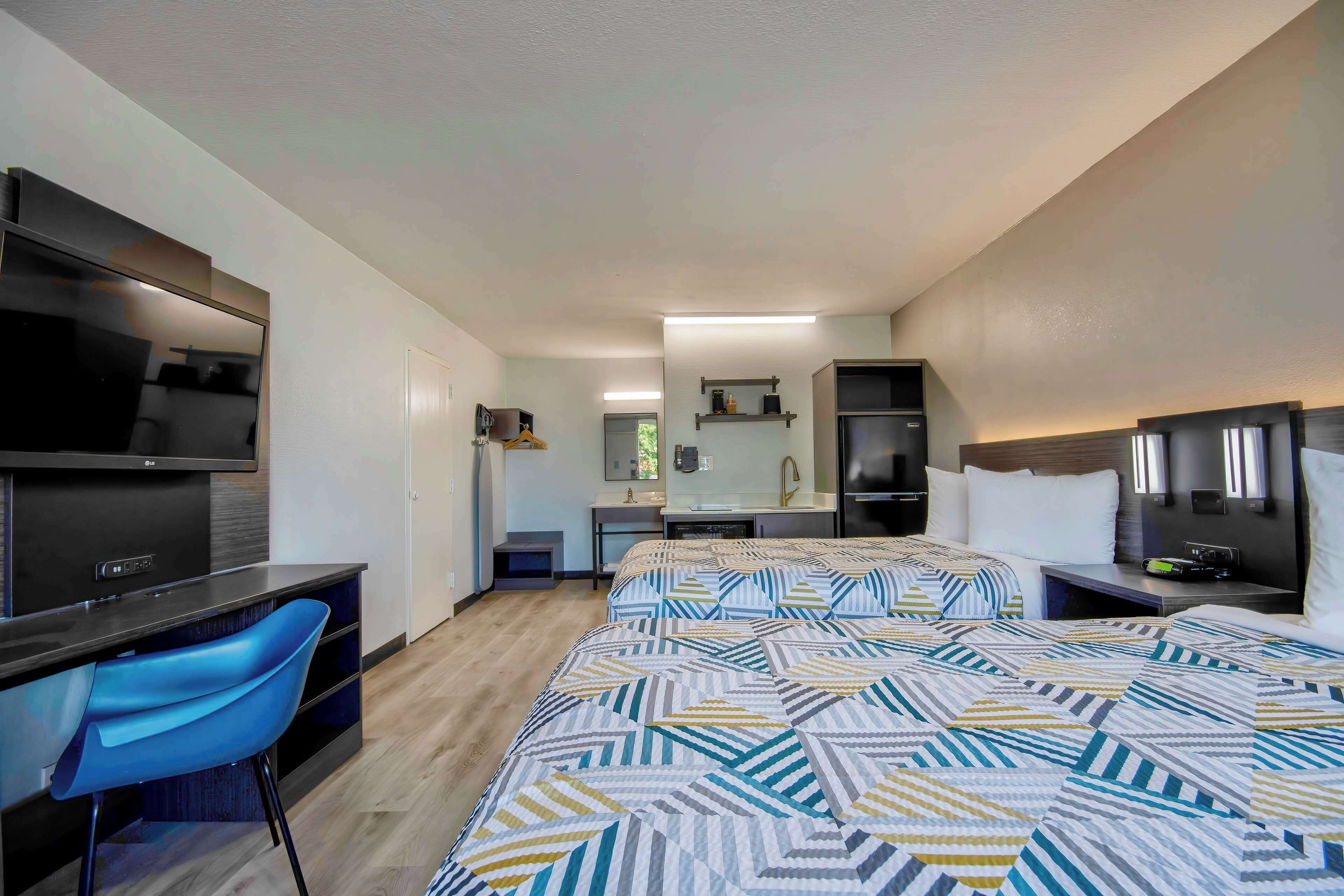 Habitación de hotel moderna con una cama grande, un escritorio con silla, televisión y un baño a la vista al fondo.