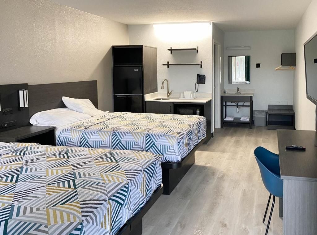 Ein Hotelzimmer mit zwei Betten, einem Schreibtisch, einem Stuhl, einer Küchenzeile und einem Badezimmer.