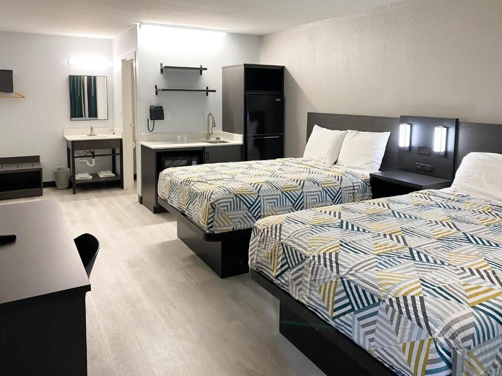 A hotel room with two beds, a desk, a chair, a small table, a mirror, a phone, and a refrigerator.