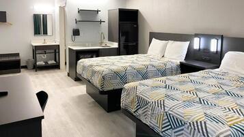 A hotel room with two beds, a desk, a chair, a small table, a mirror, a phone, and a refrigerator.