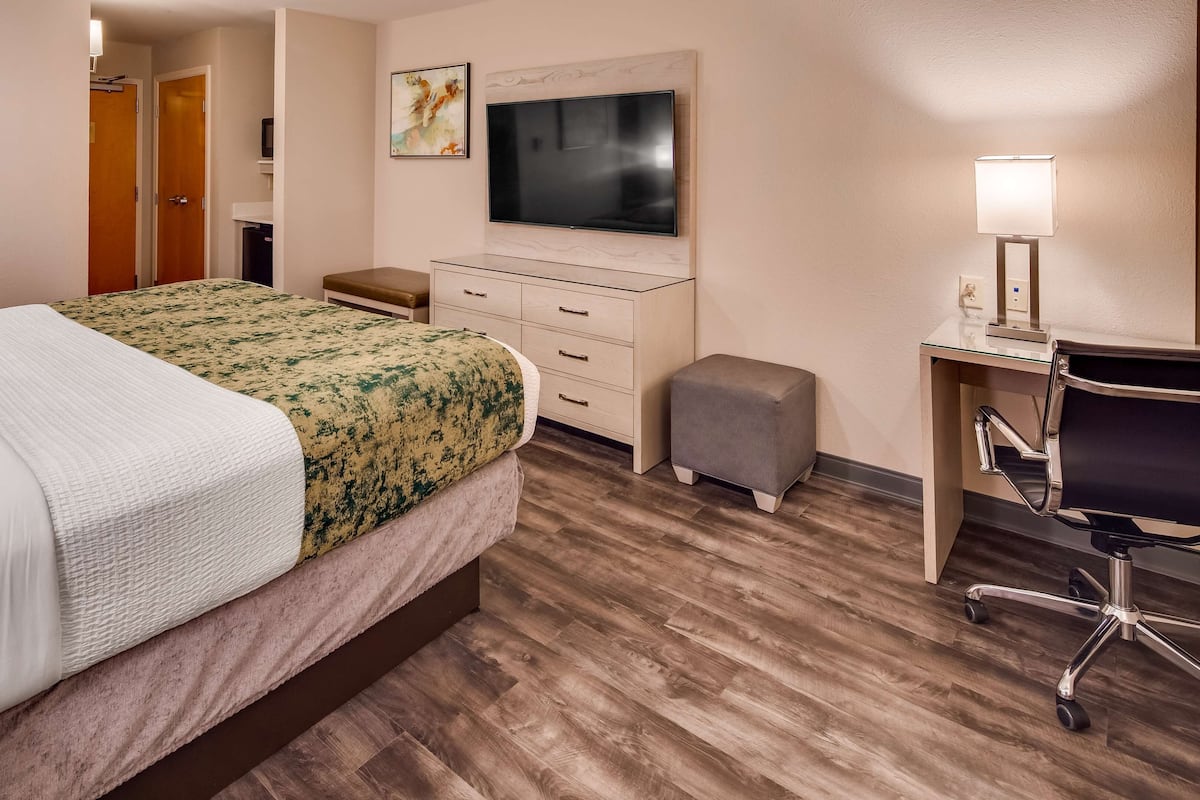 A hotel room with a bed, a desk, a chair, a TV, and a small stool.