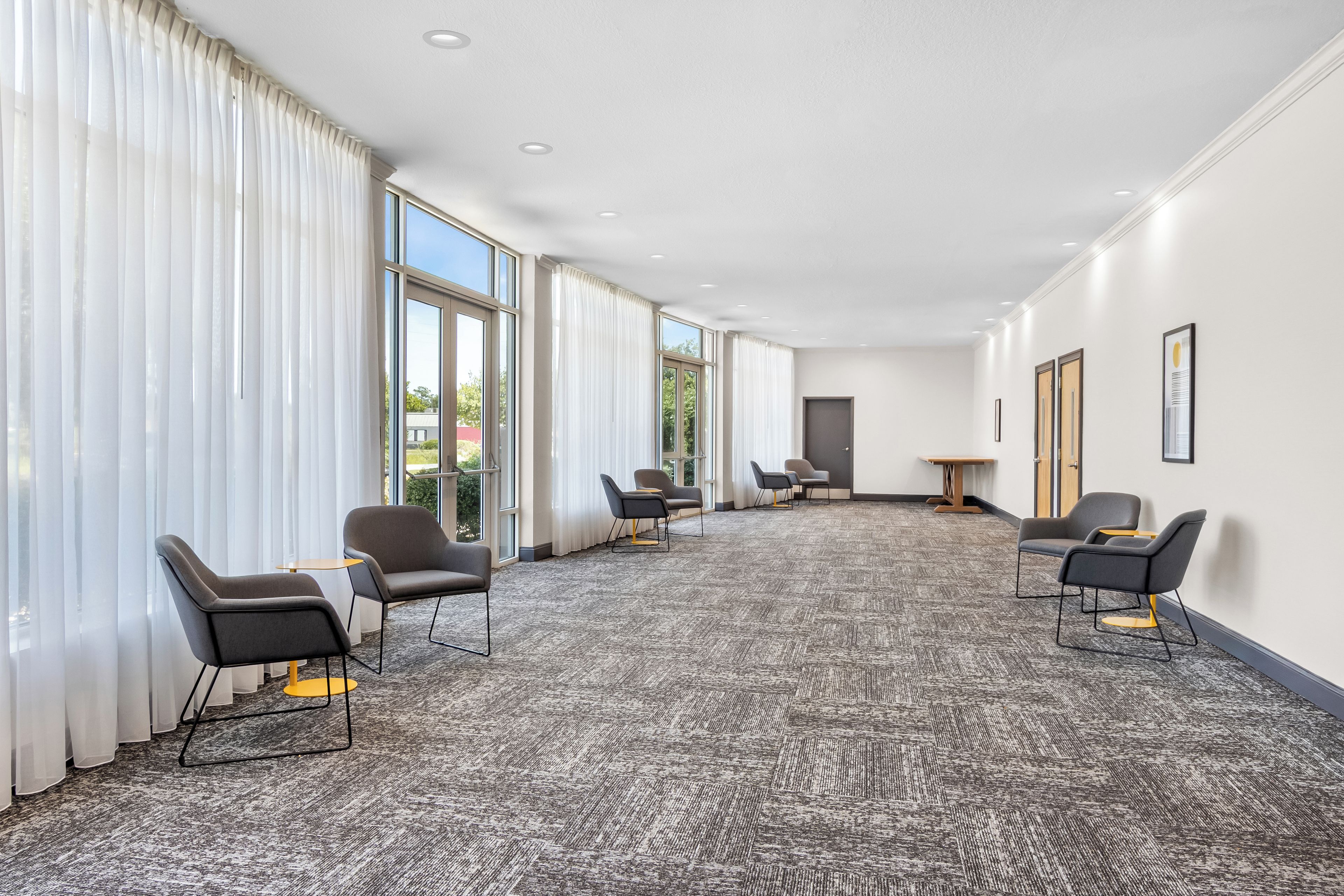 Un salón de conferencias con piso alfombrado, ventanas amplias y sillas modernas.