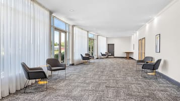 Un salón de conferencias con piso alfombrado, ventanas amplias y sillas modernas.